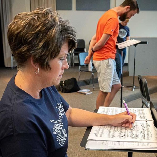 Adult music student taking notes on sheet music with two students in the background